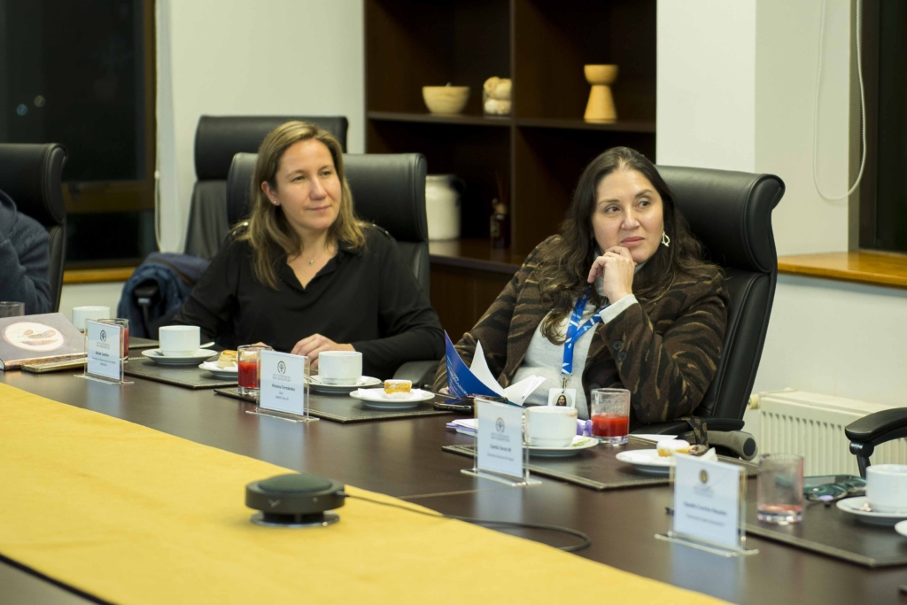 0039 - Instituto Profesional San Sebastián Two women sit at a long conference table in a meeting room, with name cards, cups, and snacks in front of them, appearing engaged in discussion.