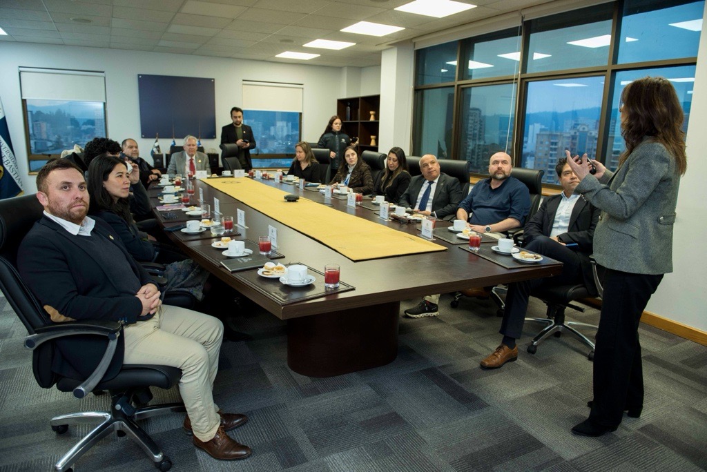 Image 36 - Instituto Profesional San Sebastián Business meeting around a long conference table with attendees listening to a presenter at the far end of the room, coffee cups and pastries on the table.