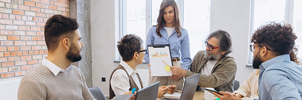 Diverse team in a meeting; a woman presents a tablet showing charts to four colleagues.